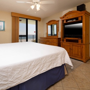 The master features a large king bed, wooden furniture, and a balcony view of the beach, complemented by a flat-screen TV