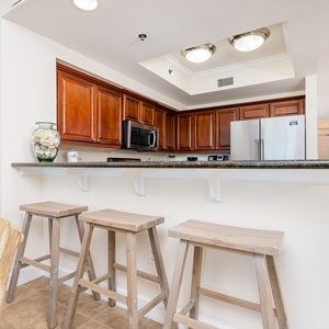 This kitchen features rich wooden cabinetry, stainless steel appliances, and a bar area with three stools for casual dining