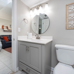 This bathroom features a stylish vanity with a round mirror, complemented by beach-themed decor and bright lighting