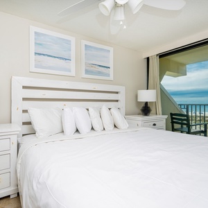 This bedroom features a plush white bed, coastal artwork, and a stunning beachfront view from the large glass doors