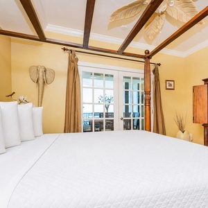 Relax in the inviting master bedroom featuring a four-poster king bed, warm decor, and view of the balcony with seating