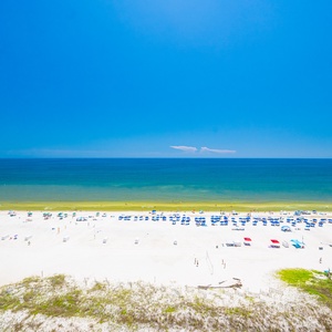 The view showcases a vibrant beach scene with colorful umbrellas and sunbathers on the soft, white sand