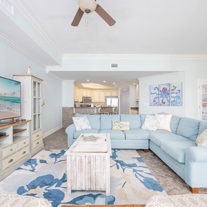 Living area featuring a cozy blue sectional with queen sleeper, large TV, and open layout leading to a modern kitchen
