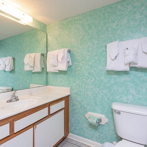 Bright turquoise walls complement the guest bathrrom with ample counter space and neatly arranged fresh towels