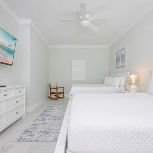 Rest in this guest room featuring two queen beds, a TV, and soft natural light