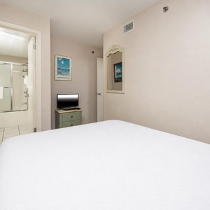 This guest room featuring a comfortable double bed, a small TV on a nightstand, and a bathroom with a glass shower