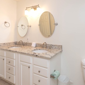 Guest bath features a dual sink vanity with a stylish countertop, two round mirrors, and soft lighting for a serene ambiance
