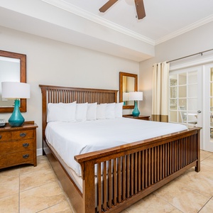 The master bedroom features a stylish wooden king bed, a bright turquoise lamp, and access to a lovely balcony view