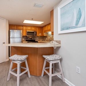 Warm wood cabinetry complements the modern kitchen's stainless appliances, featuring a breakfast bar with stylish seating