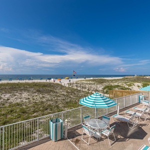 Relax on the spacious patio with striped umbrellas, overlooking the beach and vibrant beach umbrellas in the distance