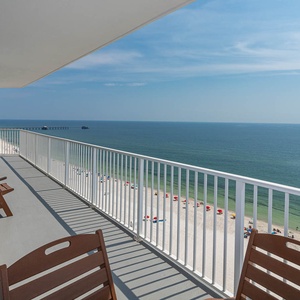 Enjoy stunning beachfront views from this expansive balcony with comfortable wooden chairs, perfect for relaxation