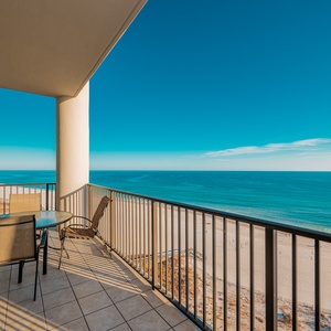 This balcony offers expansive beachfront views and features a glass table with chairs for relaxing moments outdoors
