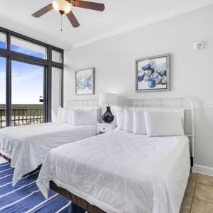 This bright bedroom features two full beds, coastal decor, and large windows offering a stunning view of the landscape