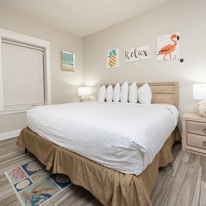 Bright and inviting guest bedroom featuring a king bed with decorative pillows, coastal-themed artwork, and warm wood accents