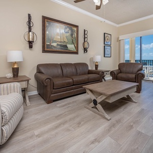 The inviting living area features a brown leather sofa with queen sleeper, accent chairs, and a balcont view of the beach