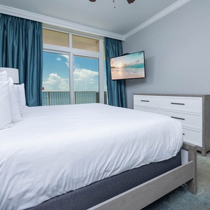Inviting master suite featuring a king bed, a TV, and large windows that frame beautiful beachfront views