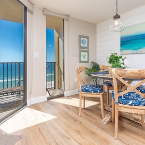 Bright dining area features a round table with blue-patterned chairs, offering a stunning view of the beach from the balcony