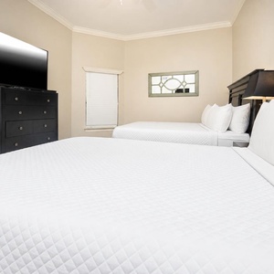 This guest bedroom features two comfortable queen beds, a wall-mounted TV, and stylish decor for a relaxing stay