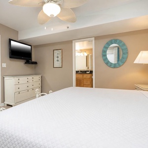 Bedroom featuring a large king bed, a mounted TV, and an en-suite bathroom with stylish decor