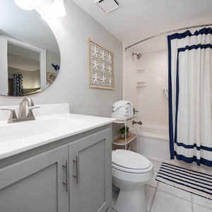 The bathroom features a sleek vanity with a spacious sink, a tub/shower combo, and coastal decor for a refreshing ambiance