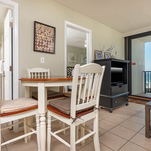 The cozy living area features a TV, a dining table for four, and a stunning beachfront view through large sliding glass doors