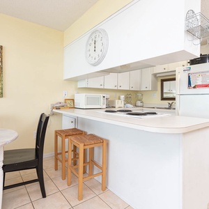 This kitchen features white cabinetry, a breakfast bar with stools, and colorful artwork, creating a cheerful cooking space