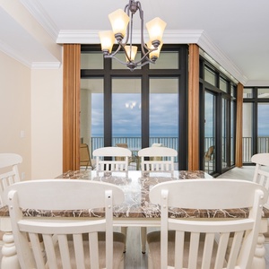 Bright dining area featuring a marble table and large windows showcasing a coastal view