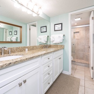 Bright master bathroom featuring a spacious granite countertop, dual sinks, and a walk-in shower with stylish tile accents