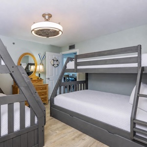 This guest bedroom features two stylish twin over full bunk beds, a charming mirror, and warm wood accents for family fun