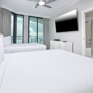 Unwind in this guest bedroom with two comfortable queen beds, a large TV, and access to a balcony for fresh air