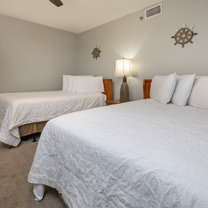 The guest bedroom features two double beds with white bedding, a bedside lamp, and a view into a bathroom area with towels