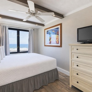 This bedroom features a cozy atmosphere with a large window offering a beachfront view and a TV for entertainment