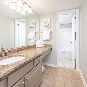 Master bathroom featuring a spacious granite countertop, neatly stacked towels, and a tub/shower combo for relaxation