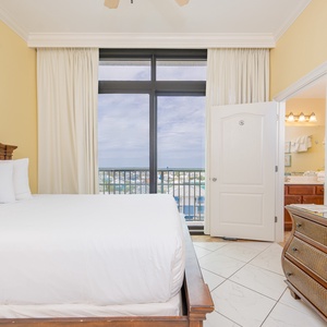 Soothing guest bedroom with a plush queen bed and a balcony showcasing a scenic coastal view