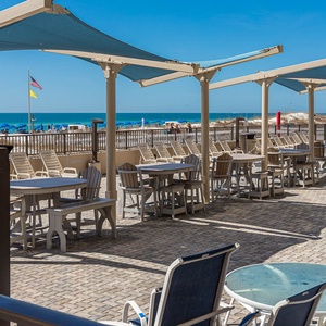 Relax at the outdoor seating area with tables and shade, just steps away from the beach and vibrant umbrellas