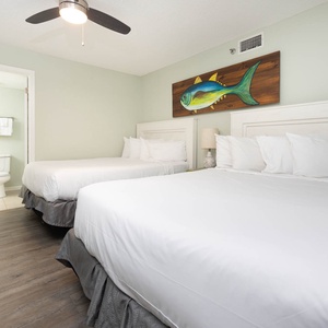 Bright guest bedroom featuring two queen beds, a ceiling fan, and a playful fish painting above a bedside lamp
