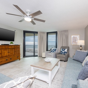 Homely living area features a large TV, comfortable seating, and stunning views of the beach through expansive glass doors