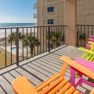 Colorful Adirondack chairs invite relaxation on the balcony, overlooking the serene beach and sparkling waters