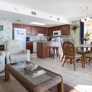 The open living area features two recliners, a glass coffee table, and a dining set surrounded by natural light