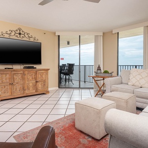 The inviting living area features a large TV, comfortable seating, and access to a balcony with a view of the beachfront