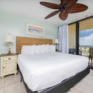 This inviting bedroom features a king bed, a ceiling fan, and a stunning beachfront view from the balcony