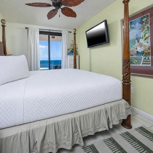 Relax in the master bedroom featuring a four-poster king bed, vibrant decor, and a beach view from the balcony