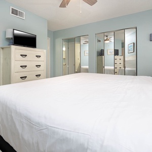 This bedroom features a comfortable bed, a flat-screen TV, and stylish mirrored cabinetry for a bright, airy feel