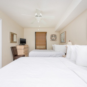 A cozy guest bedroom features two double beds, a flat-screen TV, and beach-themed artwork, creating a relaxing atmosphere