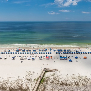 A vibrant beach scene features colorful umbrellas and loungers on soft white sand, inviting relaxation and fun by the water