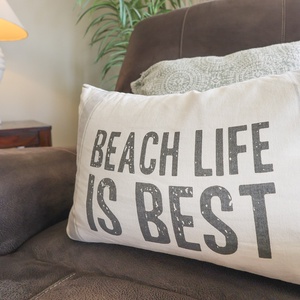 Plush seating features a decorative pillow with a beach-themed message, complemented by a stylish lamp and greenery