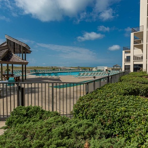 Inviting pool area features lounge chairs and a shaded gazebo, surrounded by lush greenery and a clear blue sky
