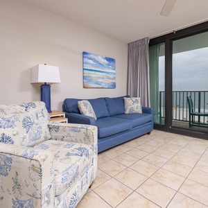 Spacious living area with comfortable seating, a vibrant beach-themed painting, and views of the balcony