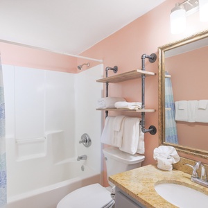 This bathroom features a stylish design with a granite countertop, open shelving for towels, and a relaxing tub shower combo
