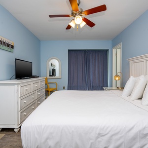 This bedroom features a comfortable bed, a TV for entertainment, and calming blue walls, creating a relaxing retreat